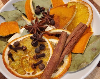 May include: A white bowl filled with dried orange slices, star anise, cinnamon sticks, bay leaves, cloves, and peppercorns. The ingredients are arranged on a wooden surface, creating a warm, inviting aesthetic. Ideal for potpourri or festive decor.