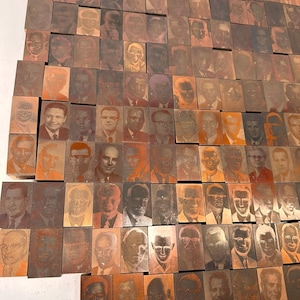 May include: A wall covered in small, rectangular copper blocks, each featuring a different engraved portrait. The portraits are in shades of brown and orange, creating a textured and artistic display.