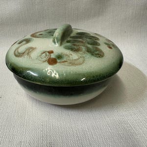 May include: A white ceramic bowl with a lid. The bowl has a green and brown glaze with a swirl pattern. The lid has a handle.