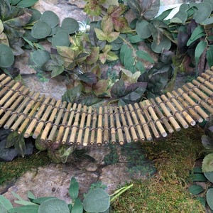 May include: A flexible suspension bridge constructed from numerous thin, light brown bamboo sticks connected by dark, thin wire. The bridge features a curved, arched shape and is positioned horizontally across the frame, showcasing a natural texture.