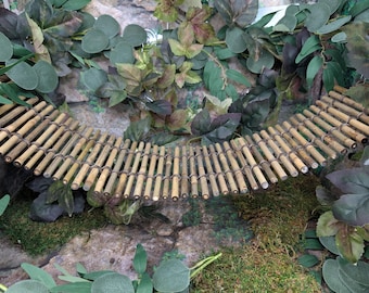 May include: A flexible suspension bridge constructed from numerous thin, light brown bamboo sticks connected by dark, thin wire. The bridge features a curved, arched shape and is positioned horizontally across the frame, showcasing a natural texture.