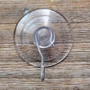 May include: A clear suction cup hook with a metal hook. The suction cup is round and has a diameter of approximately 2 inches.