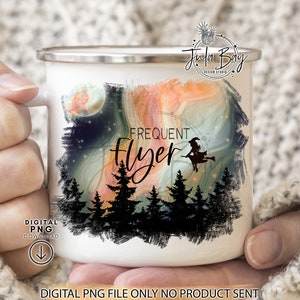 May include: A white enamel mug featuring a graphic print of a silhouette of a witch on a broomstick flying over a dark forest. The design includes a swirling orange and blue sky background with the text Frequent Flyer printed in black script.