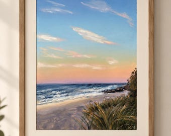 Puede incluir: Un cuadro de paisaje enmarcado que representa una playa al atardecer con cielo azul, horizonte rosa suave y nubes blancas. El primer plano muestra hierba de playa verde oscuro, mientras las olas del mar llegan a la arena. Las iniciales KM son visibles.