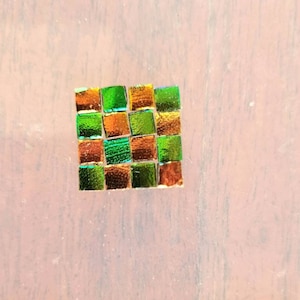May include: A small square mosaic tile made of green and gold iridescent glass tiles.