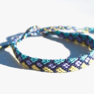 May include: A woven friendship bracelet with a geometric pattern in yellow, blue, and purple.