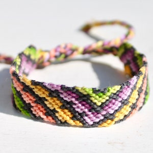May include: A colorful friendship bracelet with a chevron pattern in black, yellow, green, pink, and purple.