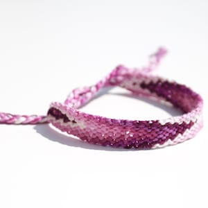 May include: A pink and white friendship bracelet with a chevron pattern.