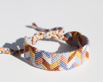May include: A woven friendship bracelet with a chevron pattern in shades of blue, brown, and yellow.
