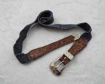 May include: A brown leather belt with a silver buckle and a denim strap. The buckle has a floral design.