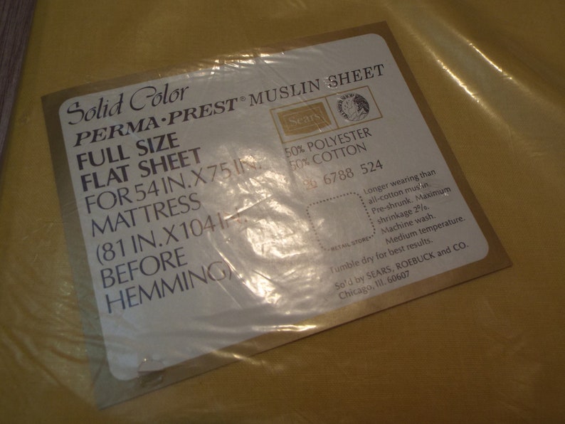 Puede incluir: Una s&aacute;bana plana de tama&ntilde;o completo en un paquete amarillo. La etiqueta dice "Solid Color PERMA-PREST MUSLIN SHEET" y enumera las dimensiones de 137 cm x 191 cm para un colch&oacute;n. La s&aacute;bana est&aacute; hecha de 50% poli&eacute;ster y 50% algod&oacute;n.