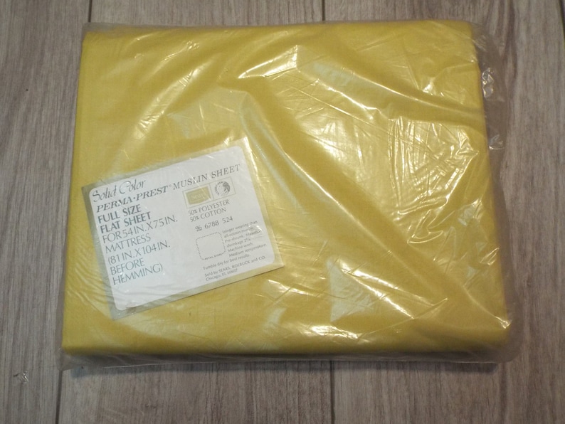 Puede incluir: Una s&aacute;bana plana amarilla, nueva y empaquetada. La s&aacute;bana est&aacute; etiquetada como "Solid Color PERMA-PREST MUSLIN SHEET" y es para un colch&oacute;n de tama&ntilde;o completo, que mide 137 cm por 191 cm. El paquete est&aacute; sellado en pl&aacute;stico transparente.