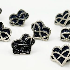 May include: A collection of nine silver-toned heart-shaped pins with a black infinity knot design. The knots are filled with black glitter.