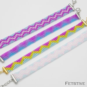 Könnte beinhalten: Vier Armbänder mit Perlen in einem Zickzackmuster in Rosa, Lila, Blau und Gelb. Jedes Armband hat einen silbernen oder goldenen Verschluss. Die Armbänder werden auf einer weißen Oberfläche präsentiert.