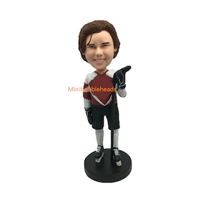 Könnte beinhalten: Eine personalisierte Bobblehead-Figur eines Hockeyspielers, der ein rot-weiß-schwarzes Trikot mit einem schwarzen Hockeyschläger trägt. Die Bobblehead-Figur steht auf einem schwarzen Sockel.