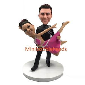 Peut inclure: Une figurine de couple en bobblehead personnalisée dansant. L'homme porte un costume noir et la femme une robe rose. La figurine est sur une base blanche.
