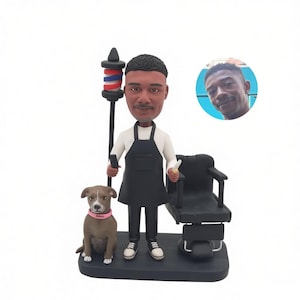 Peut inclure: Une figurine bobblehead personnalisée représentant un barbier en chemise blanche et tablier noir, debout à côté d'un poteau de barbier, d'un fauteuil de barbier noir et d'un chien marron avec un collier rose. Un médaillon montre une photo.