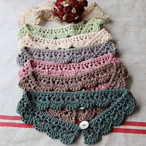 May include: A collection of handmade crochet collars in various colors, including green, cream, gray, pink, and brown. Each collar features a scalloped edge and a button closure. The collars are displayed on a neutral linen surface.