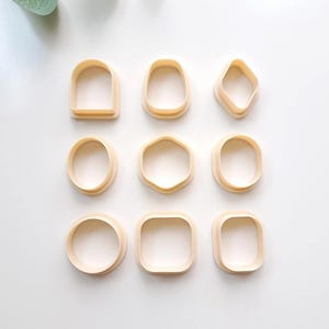 以下が含まれることがあります： 3x3のグリッドに配置された9つのライトベージュのプラスチック製クレイカッターセット。形状には、アーチ、ティアドロップ、ダイヤモンド、楕円形、六角形、角の丸い長方形、円形、角の丸い正方形、長方形が含まれています。
