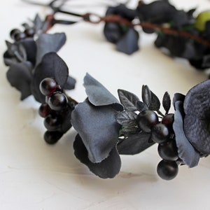 May include: Black floral crown with black berries and leaves. The crown is made of fabric flowers and is perfect for a gothic or Halloween costume.