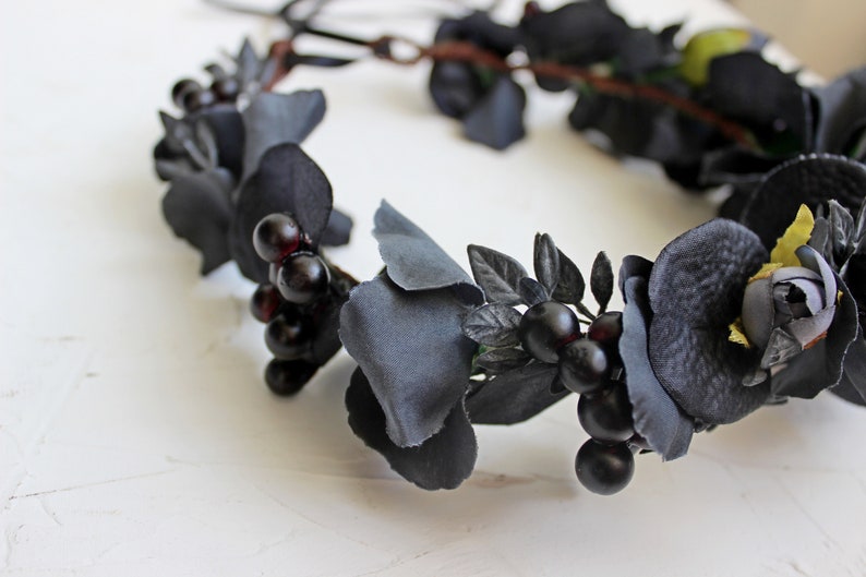 May include: Black floral crown with black berries and leaves. The crown is made of fabric flowers and is perfect for a gothic or Halloween costume.