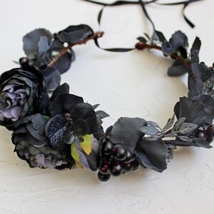 May include: A black floral crown with dark purple roses, black velvet orchids, and black berries. The crown is made with a black ribbon for tying.
