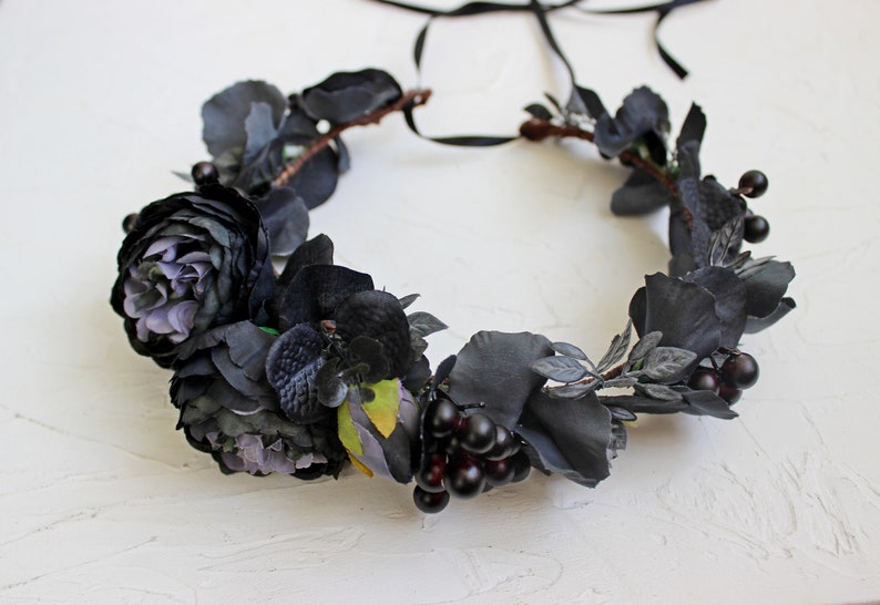 May include: A black floral crown with dark purple roses, black velvet orchids, and black berries. The crown is made with a black ribbon for tying.