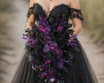 May include: A black off-the-shoulder wedding dress with lace detailing and a full tulle skirt. The bride holds a bouquet of black and purple flowers, including roses and orchids. The bouquet cascades down the front of the dress.