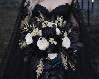 May include: A black wedding dress with a lace bodice and a long, flowing skirt. The bride holds a bouquet of black and white flowers with gold accents. A black veil drapes over the shoulders. A candelabra with lit candles is in the background.