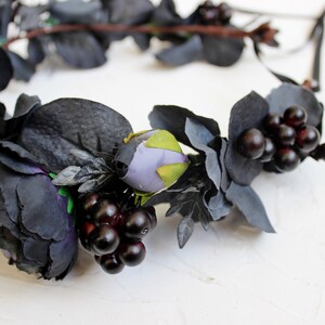 May include: A black floral crown with dark purple and green flowers and black berries.