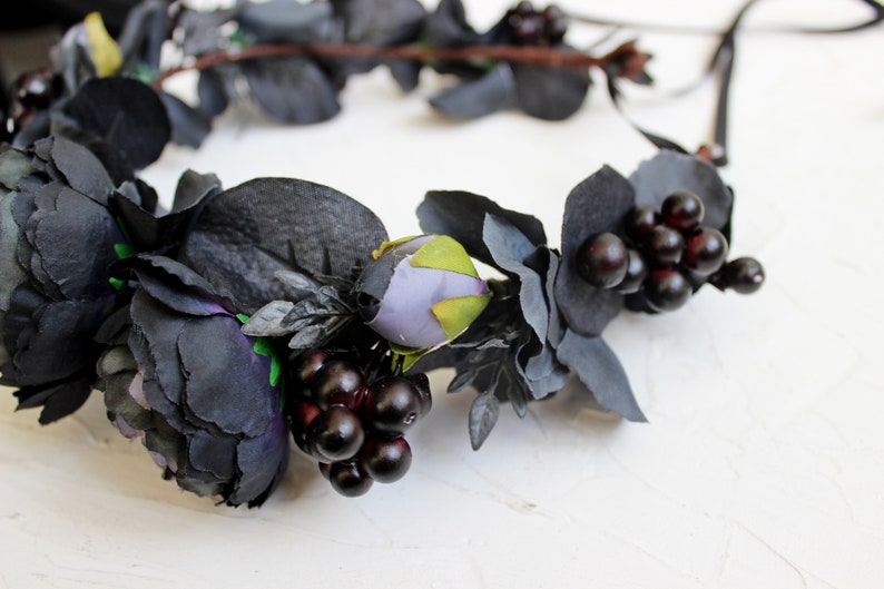 May include: A black floral crown with dark purple and green flowers and black berries.