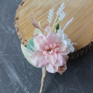 Puede incluir: Un boutonniere de flor rosa con acentos blancos y vegetaci&oacute;n, atado con cuerda.