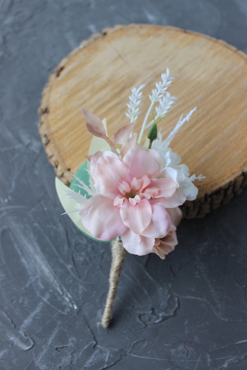 Puede incluir: Un boutonniere de flor rosa con acentos blancos y vegetaci&oacute;n, atado con cuerda.