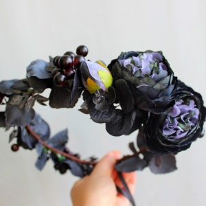May include: A black floral crown with purple flowers and dark red berries. The crown is made of artificial flowers and leaves.