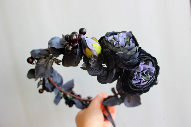 May include: A black floral crown with purple flowers and dark red berries. The crown is made of artificial flowers and leaves.