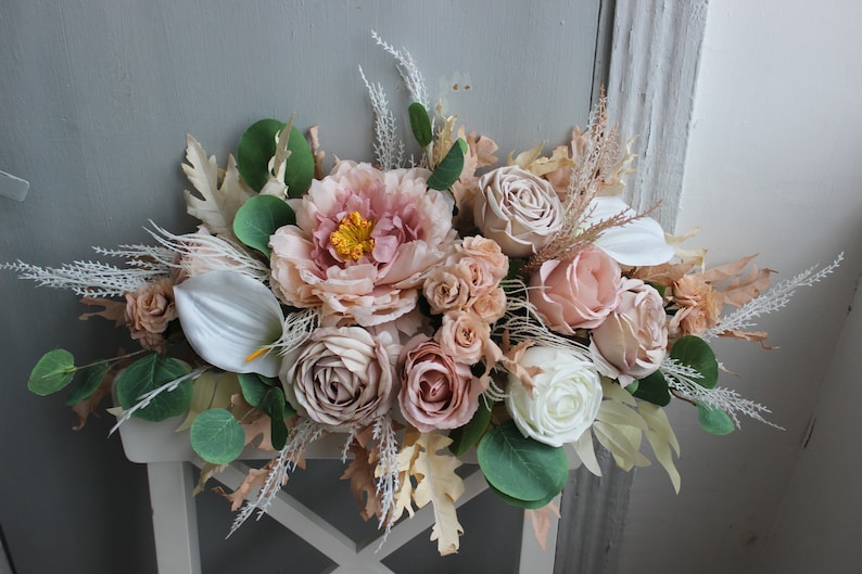 Puede incluir: Un arreglo floral en tonos rosa y blanco con hierbas secas y vegetaci&oacute;n. El arreglo incluye peon&iacute;as, rosas y otras flores.