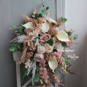 Puede incluir: Un ramo de novia en cascada con rosas de color rosa claro, blancas y crema, eucalipto y hierbas secas. El ramo est&aacute; dispuesto en forma de l&aacute;grima y es perfecto para una boda r&uacute;stica o bohemia.