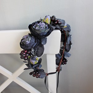 May include: A dark purple and black floral crown with burgundy berries. The crown is made of silk flowers and is tied with a black ribbon.