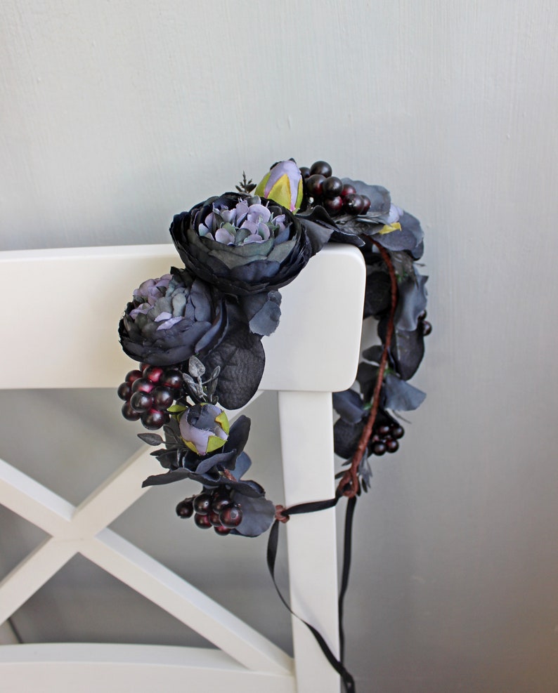 May include: A dark purple and black floral crown with burgundy berries. The crown is made of silk flowers and is tied with a black ribbon.