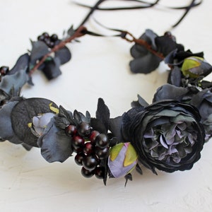 May include: A black floral crown with dark purple berries and black fabric flowers. The crown is made with a brown wire base and has black ribbon ties.