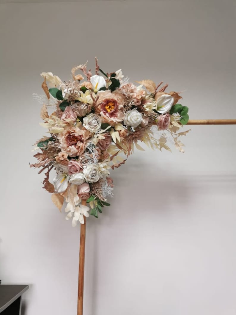 Puede incluir: Un arco de madera decorado con un arreglo floral de flores secas en tonos crema, beige y rosa. Las flores incluyen rosas, peon&iacute;as y otras flores delicadas.