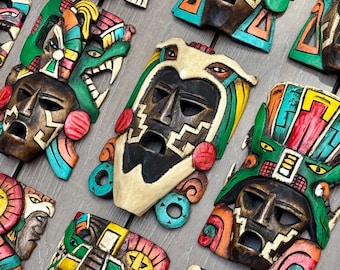 May include: A collection of vibrantly painted wooden masks with intricate designs. The masks feature various colors, including red, green, blue, and yellow, and depict stylized faces and patterns. The text "RAMPOS MX" is visible in the lower left corner.