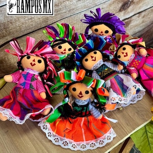 May include: A selection of traditional Mexican rag dolls. Each doll has a round face, black hair, and a colourful dress. The dolls are decorated with ribbons and lace, displaying bright shades of pink, orange, green, and purple.