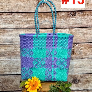May include: A tote bag featuring a woven plastic pattern in alternating purple and teal squares. The bag has two braided handles in matching purple and teal colors. The number #13 is printed in red on a white square in the upper right corner.