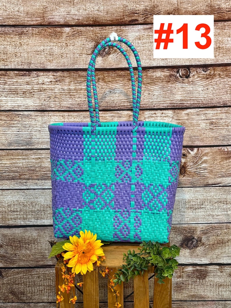 May include: A tote bag featuring a woven plastic pattern in alternating purple and teal squares. The bag has two braided handles in matching purple and teal colors. The number #13 is printed in red on a white square in the upper right corner.