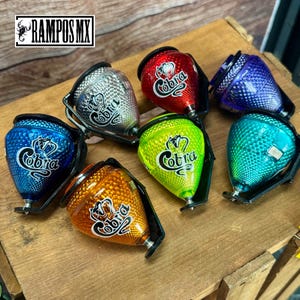 K&ouml;nnte beinhalten: Eine Sammlung farbenfroher Kreisel mit dem Wort "Cobra" und einem Schlangenlogo. Die Kreisel sind in verschiedenen Farben erh&auml;ltlich, darunter Silber, Rot, Blau, Gr&uuml;n und Orange. Die Kreisel bestehen aus einem gl&auml;nzenden Material und haben eine strukturierte Oberfl&auml;che.