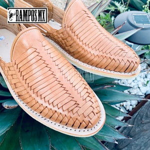 May include: A pair of tan leather sandals with a woven design. The sandals have a white sole and are made in Mexico.