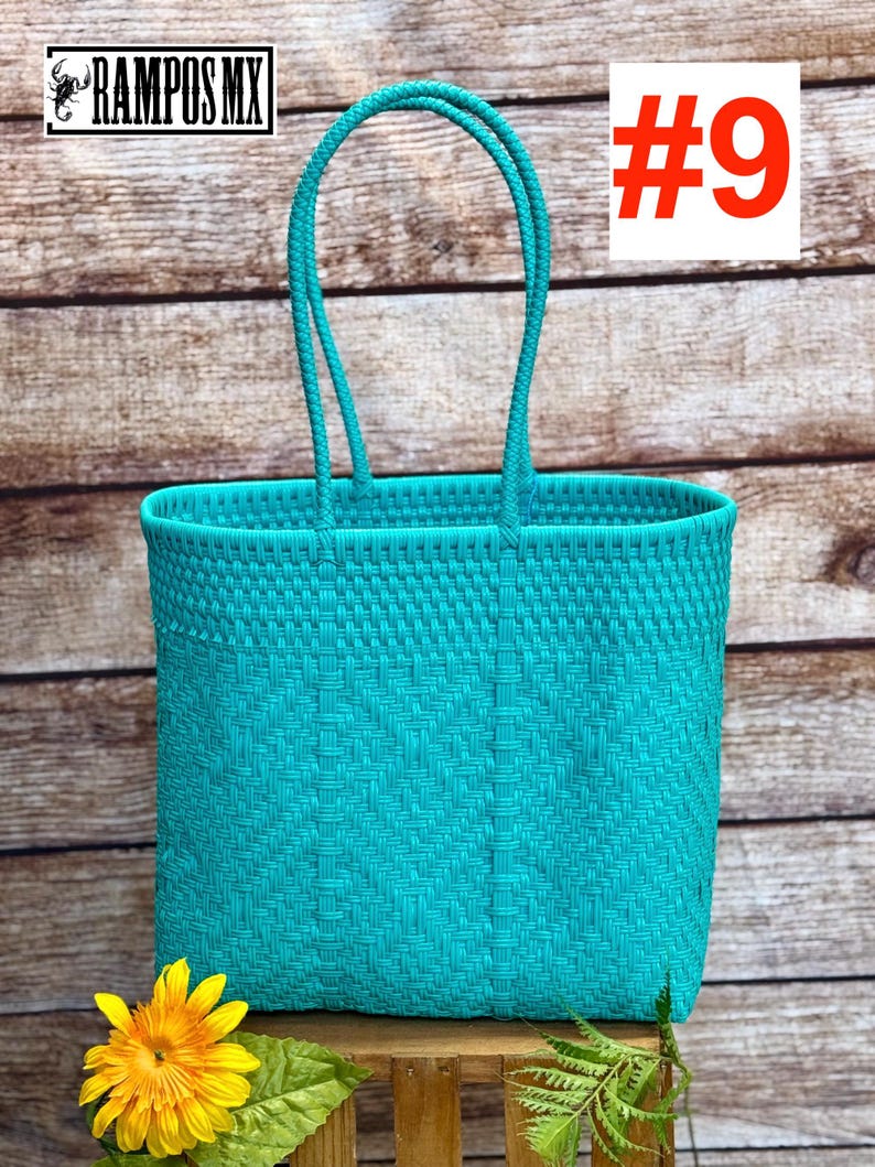 May include: A bright turquoise woven tote bag featuring a structured rectangular body and two matching arched handles. The bag displays a consistent basket-weave pattern throughout its surface. The text RAMPOS MX and the number #9 are visible.