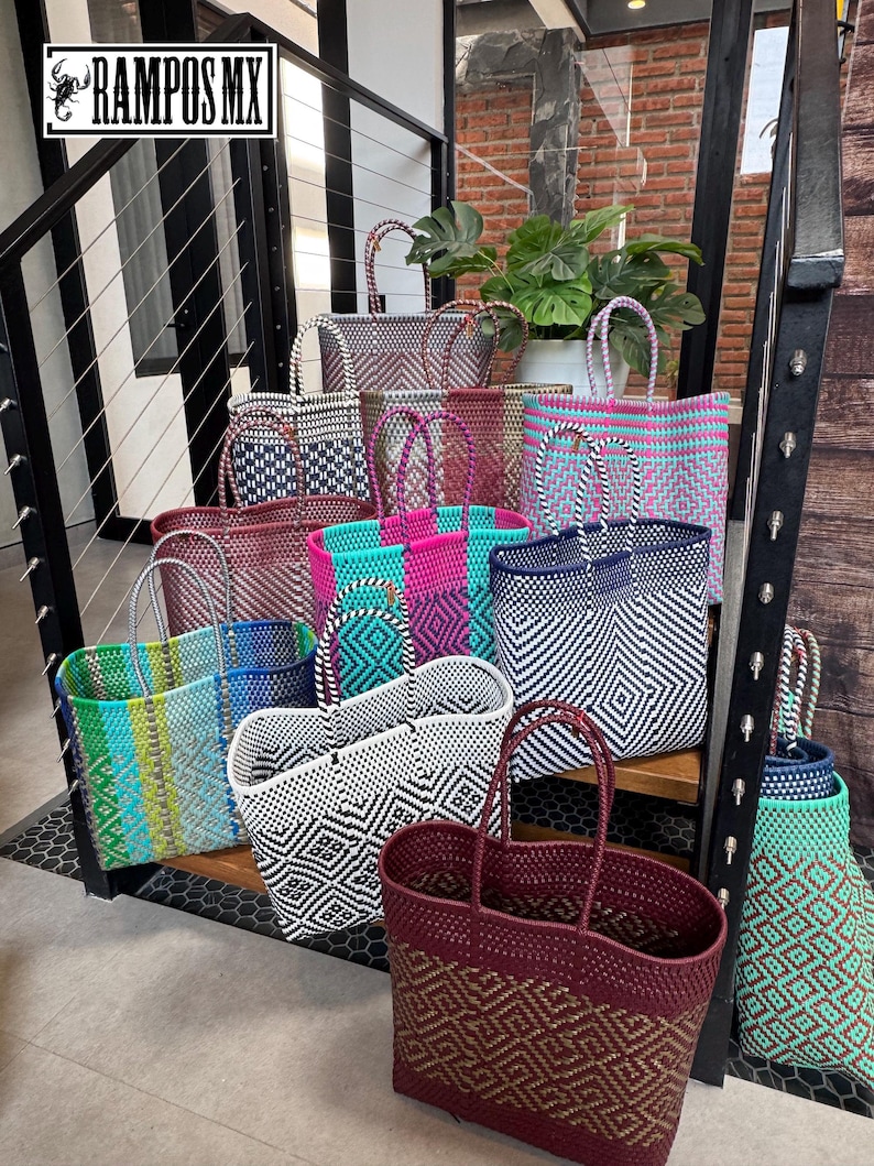 May include: A collection of woven plastic tote bags in various colors and geometric patterns, including blue, pink, white, black, and brown. Each bag features two handles and a rectangular base. A logo with the text RAMPOS MX is visible.