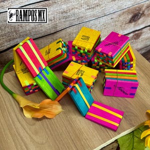 Könnte beinhalten: Eine Sammlung farbenfroher Holzspielzeuge, darunter gestapelte und verbundene Teile, in Gelb-, Rosa-, Grün- und Blautönen. Einige Teile sind zu einer Linie angeordnet. Die Spielzeuge tragen die Aufschriften "Mexico" und "Rampas MX".